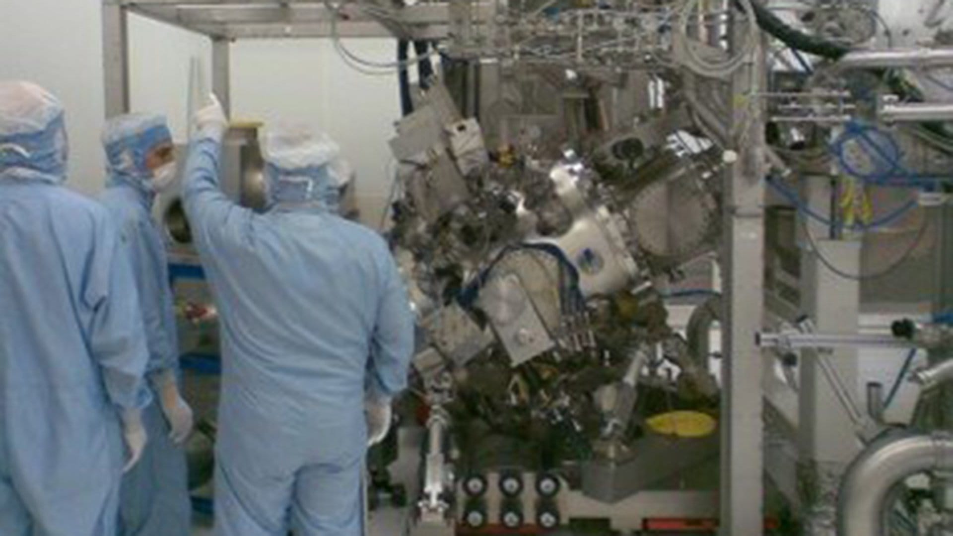 Three cleanroom engineers standing next to a Cymer EUV light source