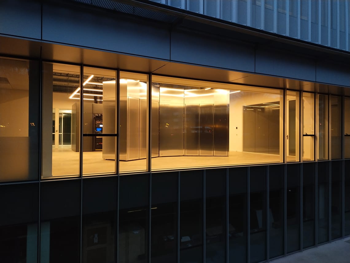 A quantum computer enclosure lit up behind the glass front of an office building at dusk