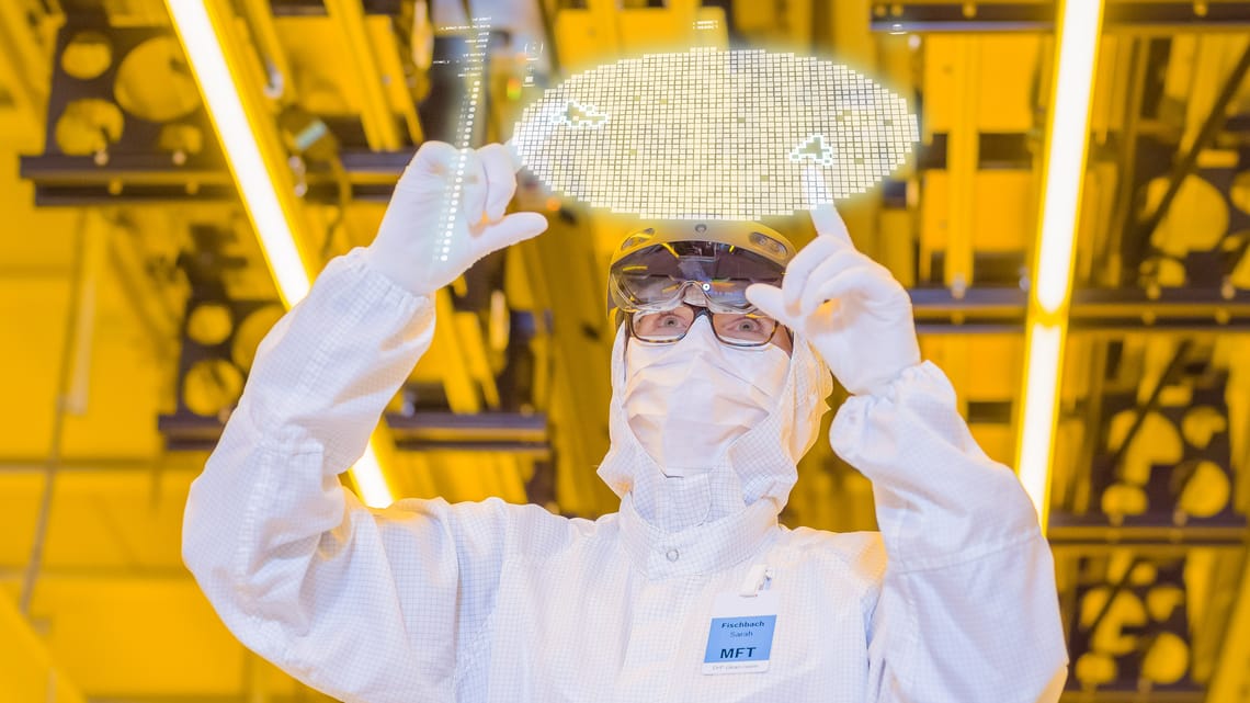 Cleanroom worker holding a silicon wafer under yellow lighting at Bosch’s Dresden semiconductor factory.